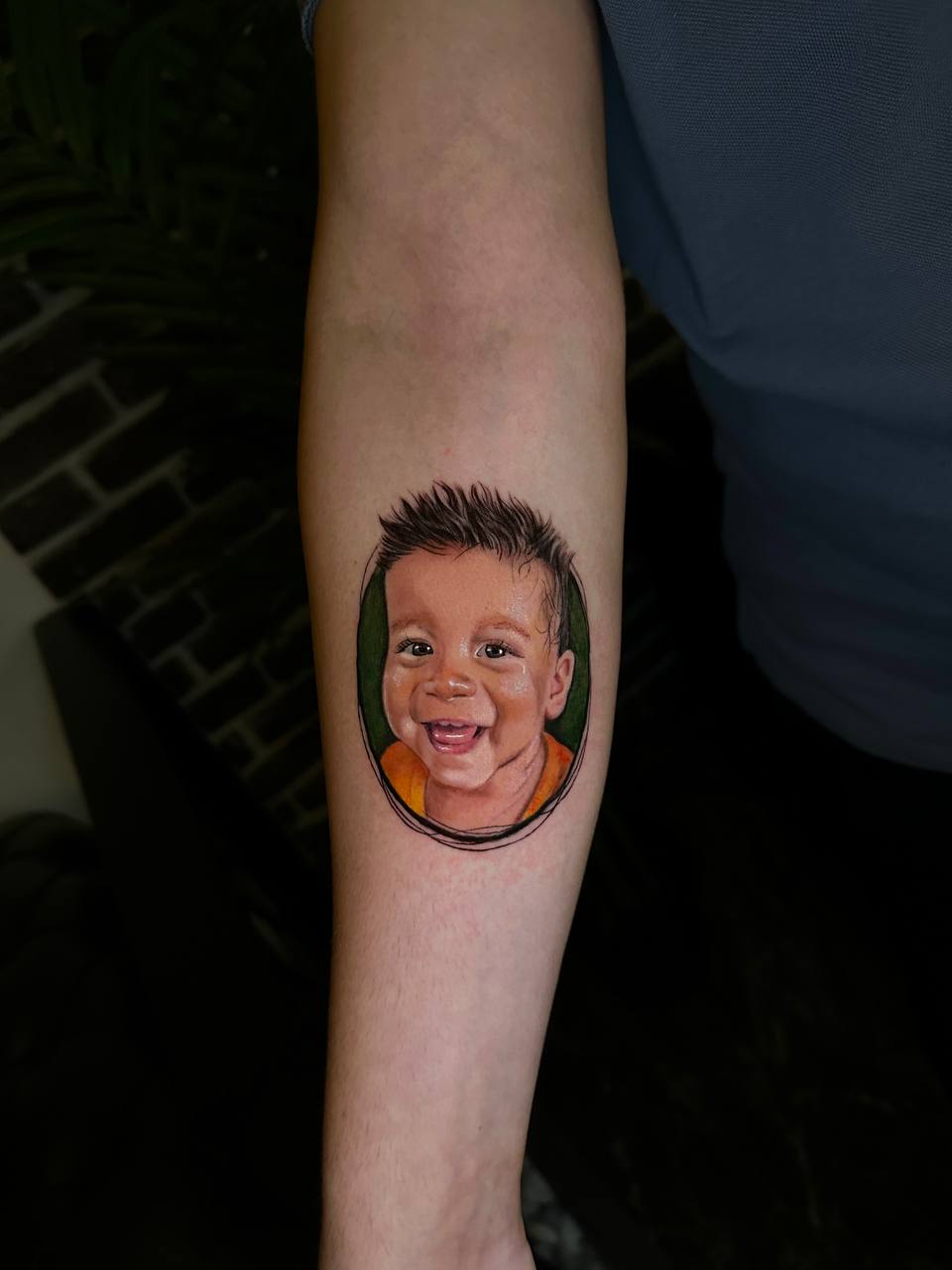 Tattoo eines lachenden Kindes auf dem Arm, bunte Details, fröhlicher Ausdruck.