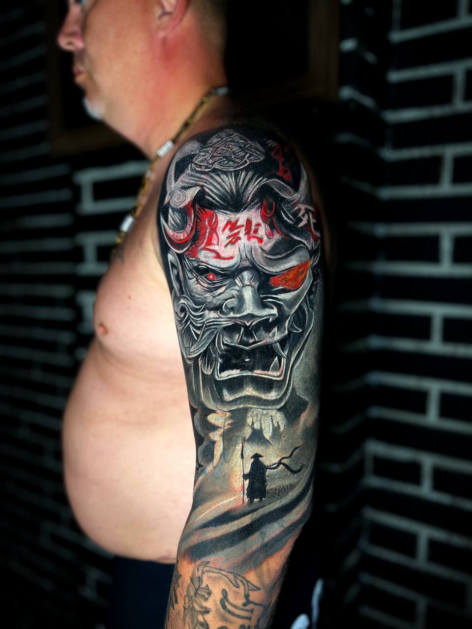 Rückansicht eines Mannes mit einem eindrucksvollen, detaillierten Dämonentattoo am rechten Arm, schwarz-rot.
