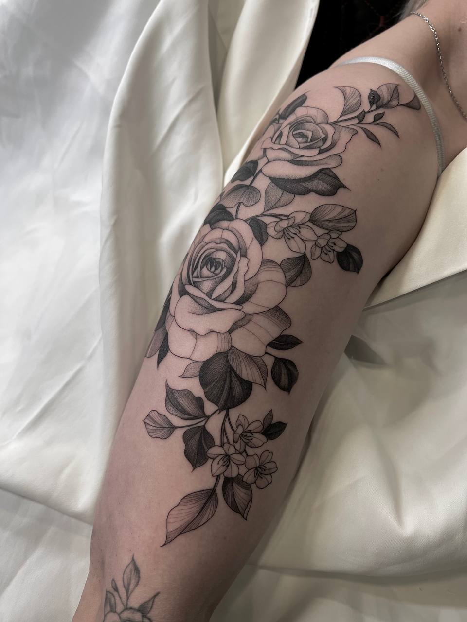 Schwarz-graues Rosentattoo auf einem Arm, elegant im weißen Stoffumschlag.