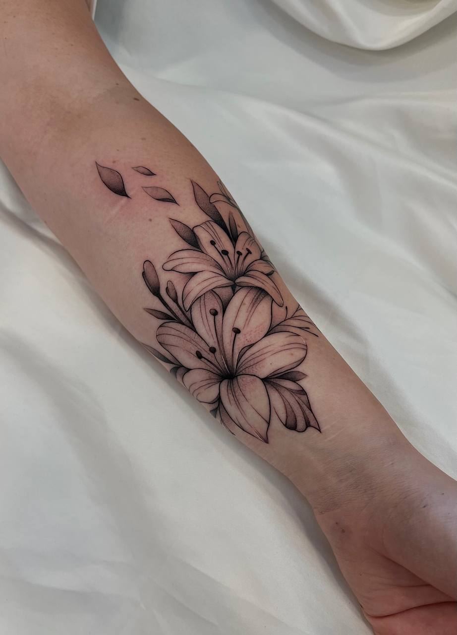 Ein Arm mit einem schwarz-weißen Lilien-Tattoo auf hellem Stoffhintergrund.