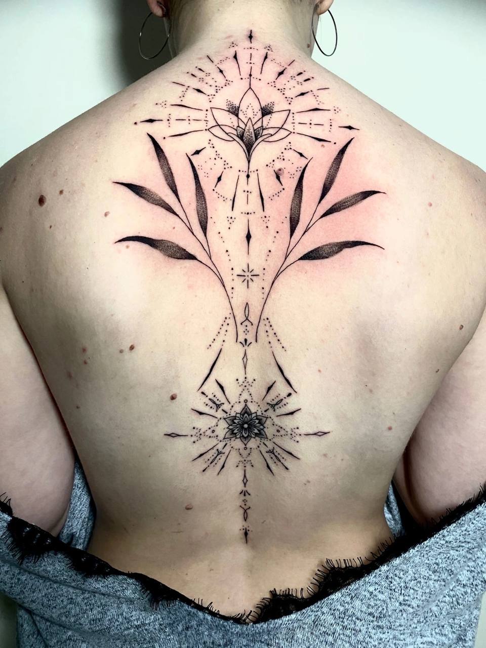 Rücken mit schwarzem Mandala-Tattoo und floralen Details, Person mit kurzen Haaren, entspannte Haltung.