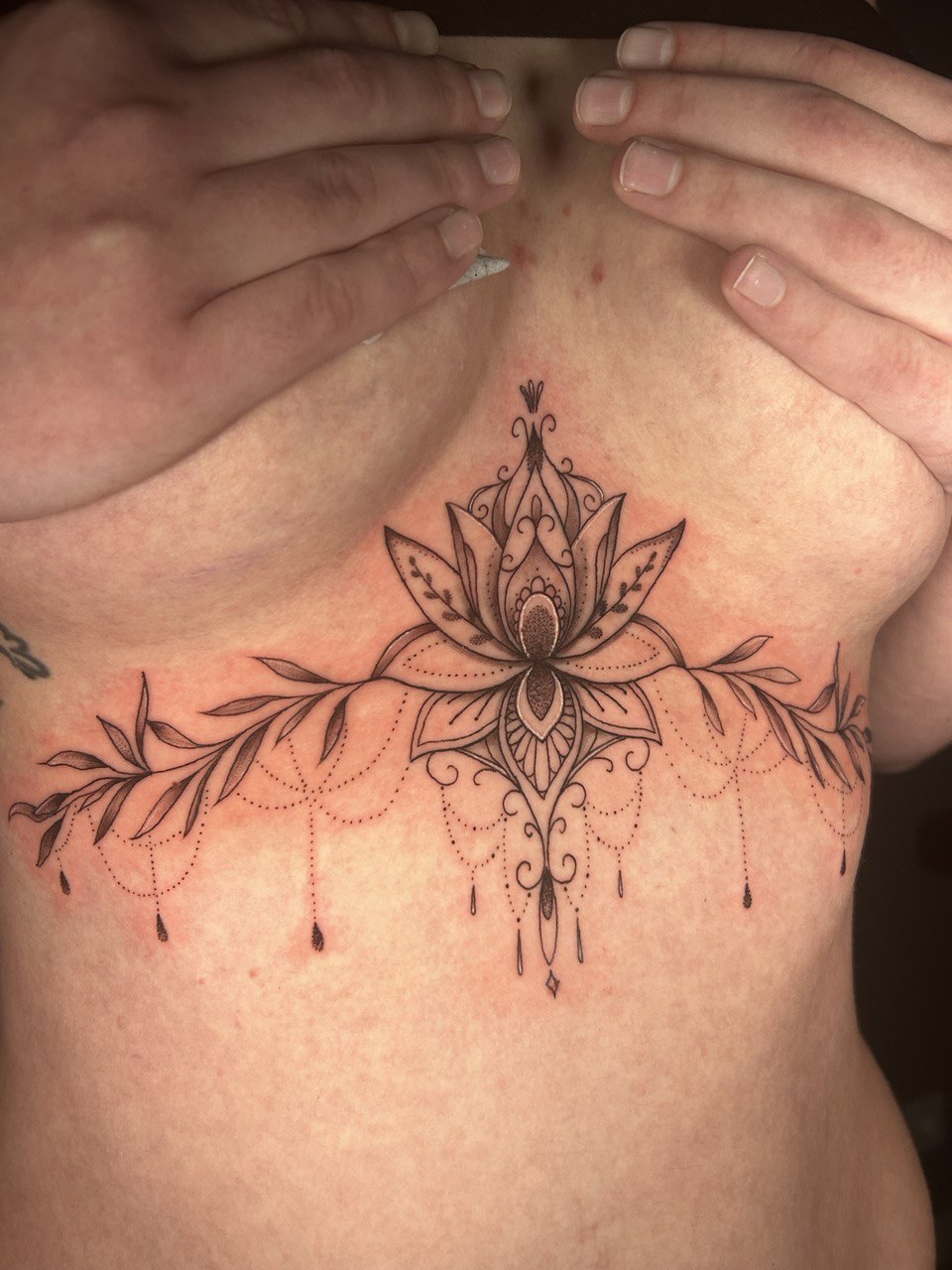 Person mit erstaunlichem floralen Brusttattoo, detailliert schwarz, Hände verdecken Oberteil.