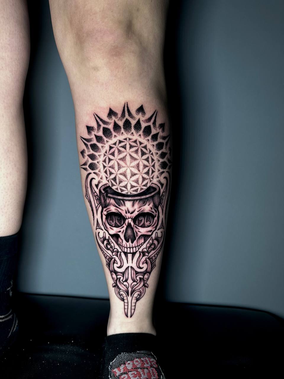 Bein mit detailliertem Totenkopf-Tattoo, schwarzes und graues Design, komplexe Muster.