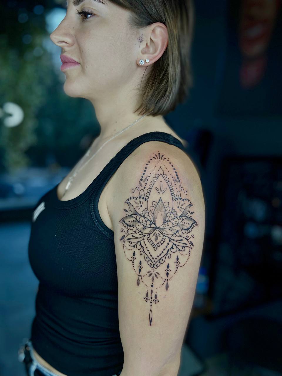 Frau im Profil mit neutralem Gesichtsausdruck, trägt ein schwarzes Top, dekoratives Tattoo am Arm.