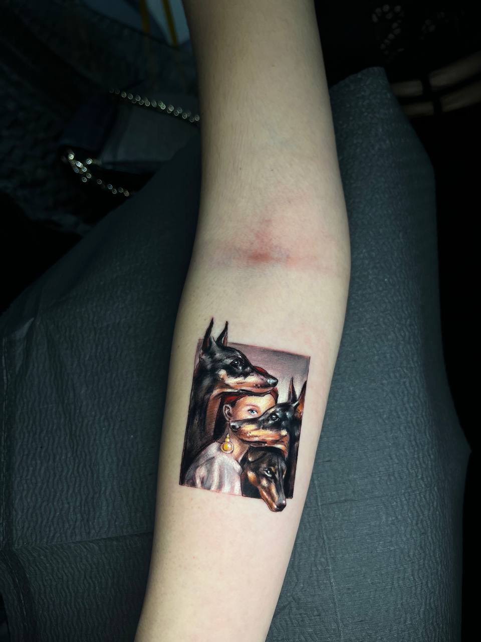 Tattoo auf dem Arm zeigt Frau mit Hundeköpfen, realistische Farben, detailliertes Design.