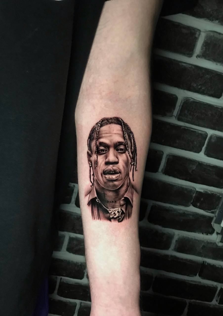 Tattoo eines Mannes mit Zöpfen und neutralem Gesichtsausdruck auf dem Unterarm, Hintergrund Backstein.
