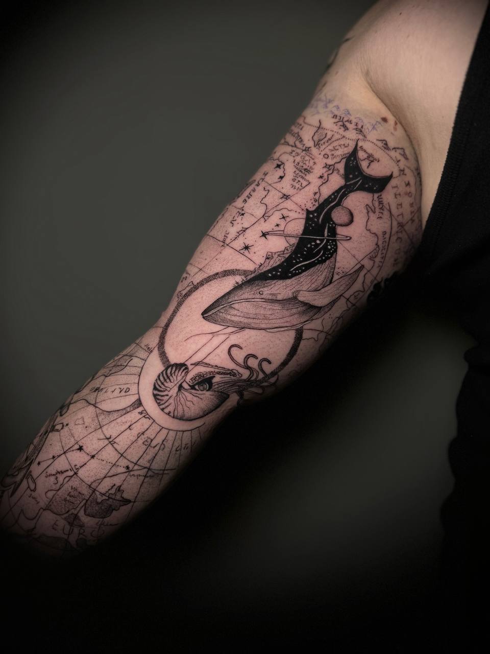 Tätowierter Arm mit Seekarte, Wal und Nautilus, Schwarz-Weiß, detaillierte Linienarbeit.
