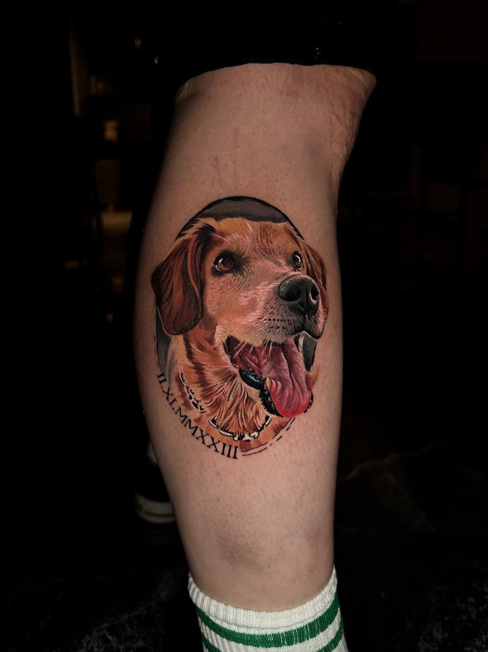 Ein realistisch tätowierter Hund auf einem Bein, fröhlich mit heraushängender Zunge.