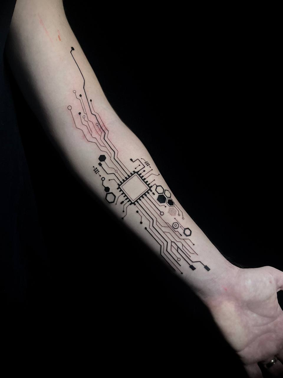 Unterarm mit schwarzem Tattoo eines Schaltkreises auf heller Haut.