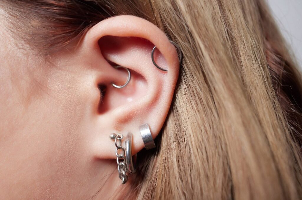 Nahaufnahme eines menschlichen Ohrs mit mehreren Ohrpiercings und blonden Haaren.