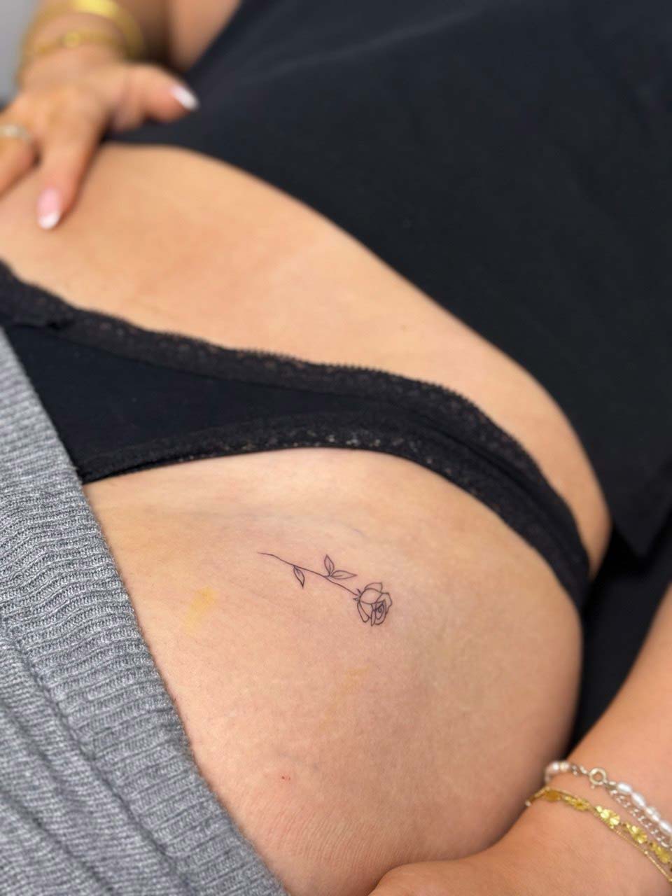 Person mit schwarzem Top, kleiner Rose-Tattoo im Hüftbereich, entspannt.