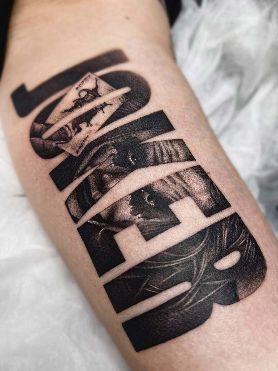 Tätowierung auf einem Arm mit Porträt und Text, schwarz-weiß, mit geometrischem Design.