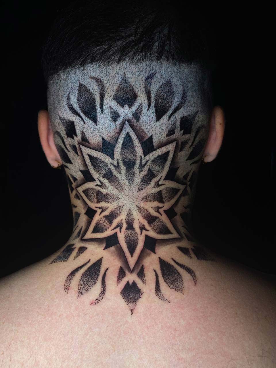 Kopf eines Mannes mit geometrischem Tattoo am Hinterkopf, schwarze und graue Töne.