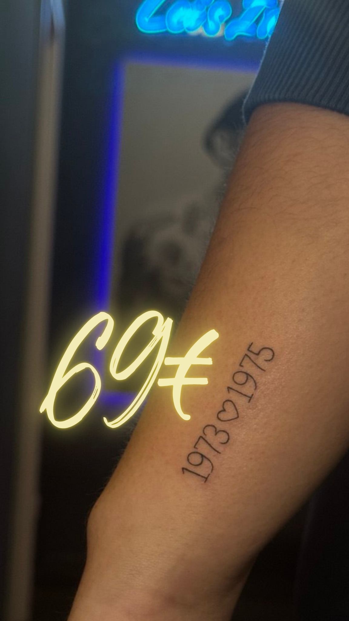 Ein Arm mit einer Tätowierung "1973 ♥ 1975" und leuchtendem "69€“-Symbol.